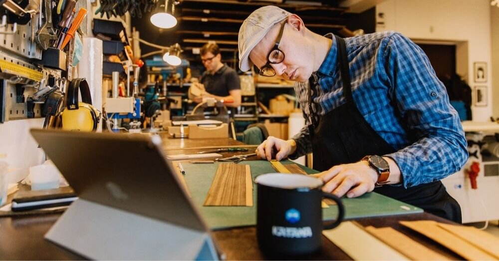 Framed by Karl uses a job shop manufacturing set-up. In the foreground, an employee prepares material whilst in the background at another workstation an employee shapes a product.